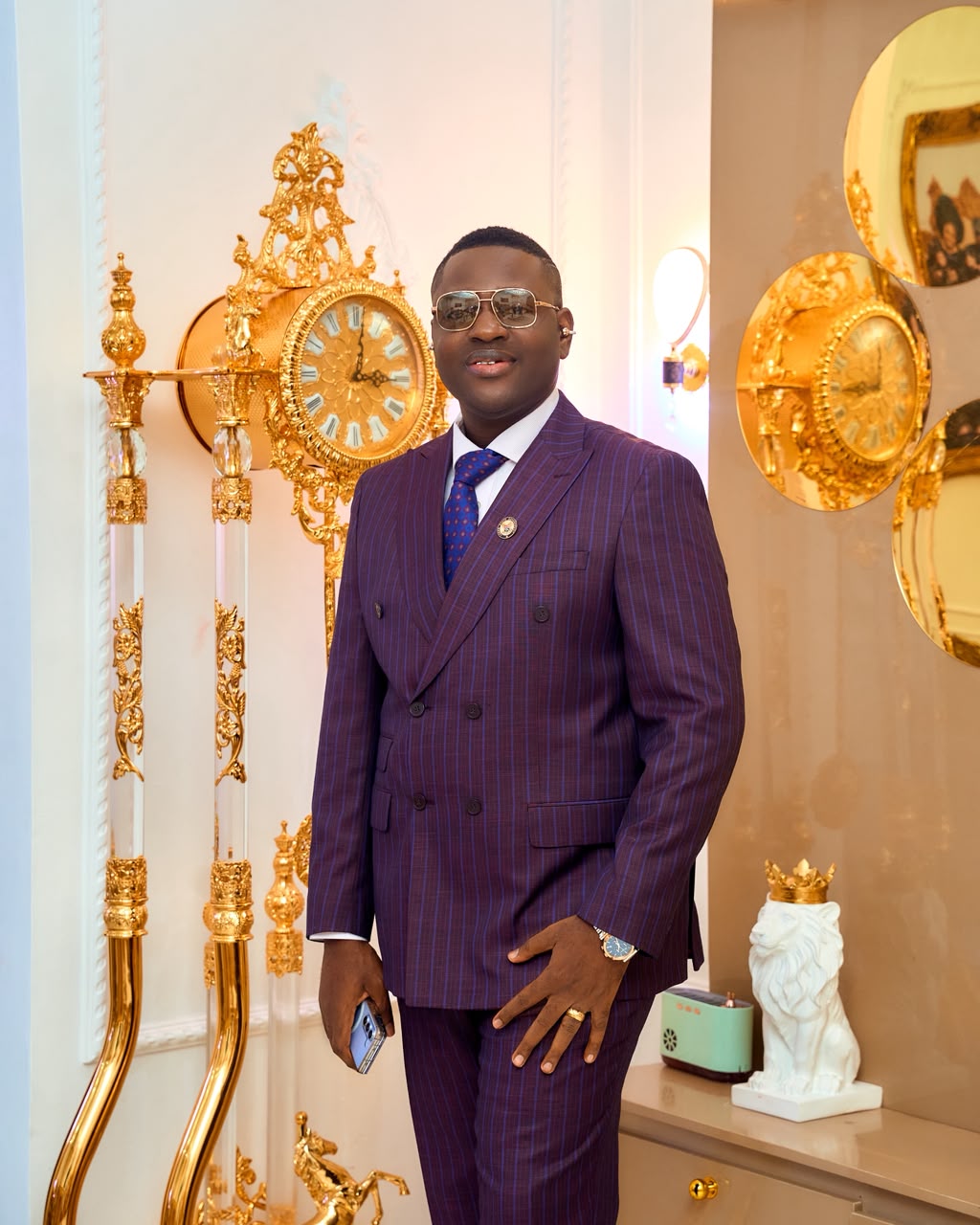 Prince Fuhad Oloto in sunglasses beside gold ornamental clocks